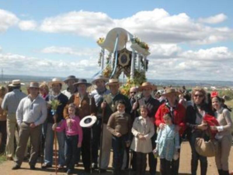 Grupo de personas en trajes tradicionales posando junto a un carro de madera decorado con flores en un paisaje rural.
