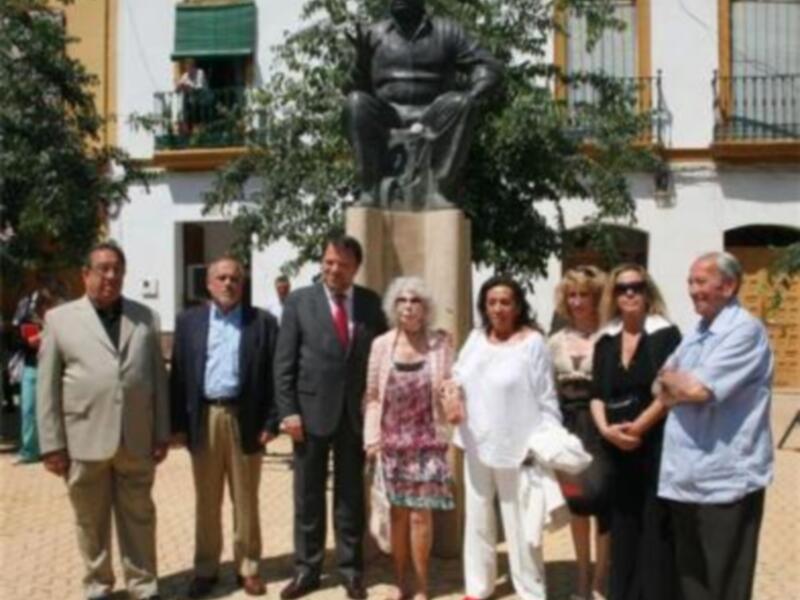 Grupo de personas posando frente a una estatua en un entorno urbano con edificios históricos al fondo.