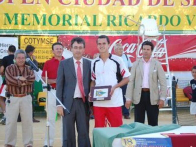 Equipo de fútbol celebrando el título en un torneo de la Ciudad de Sevilla, con un trofeo en la mano y una bandera de Coca-Cola al fondo.
