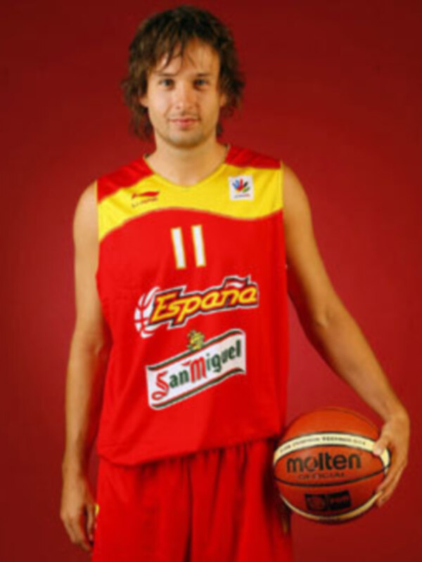 Un hombre con cabello largo y rizado, vestido con una camiseta roja y amarilla que lleva el nombre "España" y la marca de cerveza San Miguel, sostiene un balón de baloncesto con la marca "Molten". El fondo es rojo.