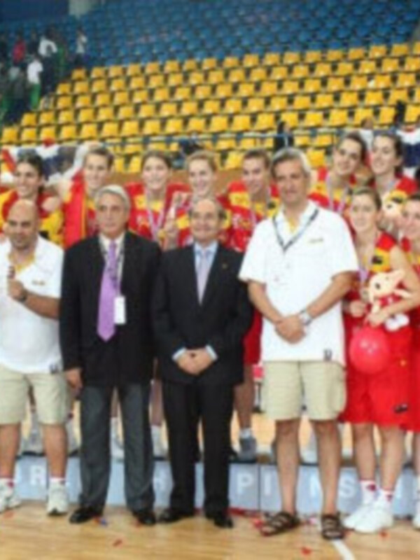 Equipo de baloncesto celebrando con banderas y medallas en un estadio vacío.