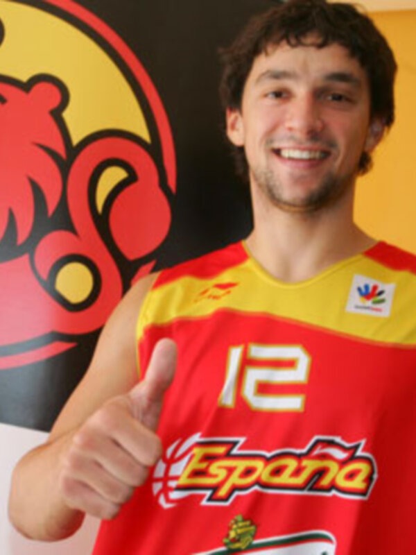 Un hombre sonríe y da un pulgar hacia arriba, vestido con una camiseta roja y amarilla con el número 12 y la palabra 'España' en el pecho.