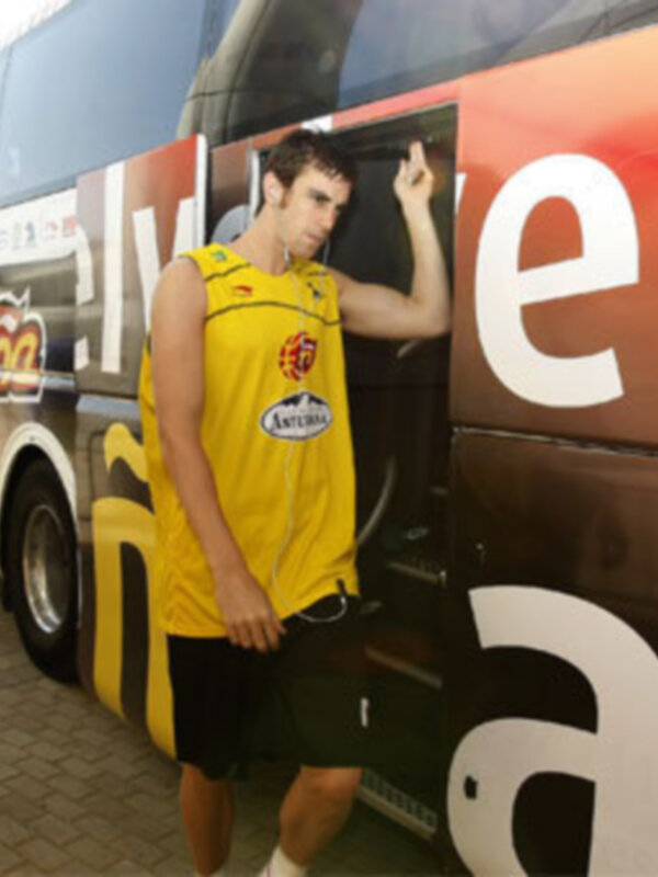 Un hombre en una camiseta amarilla y pantalones cortos negros está bajando del lado izquierdo de un autobús grande con anuncios en rojo y blanco.