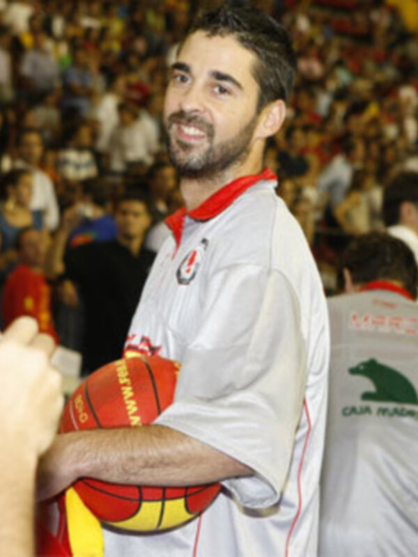 Un hombre con una camiseta blanca y roja, posando para una foto en un estadio lleno de espectadores.