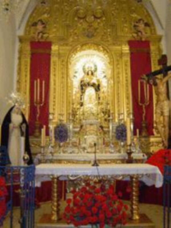 Altar dorado con estatua central, flores rojas y velas.