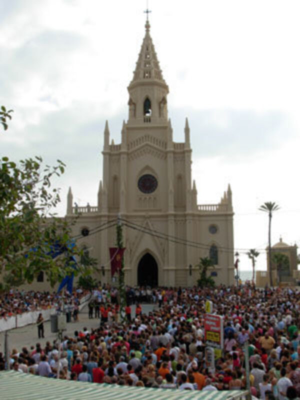 Una gran iglesia con una torre alta y un reloj en la parte superior, rodeada de una multitud de personas. La imagen muestra un cielo nublado y árboles en el frente de la iglesia.