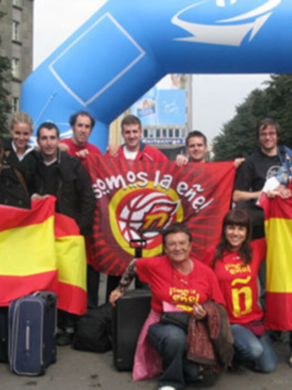 Gente con banderas españolas y un arco azul en el fondo, posiblemente en una celebración o evento público.
