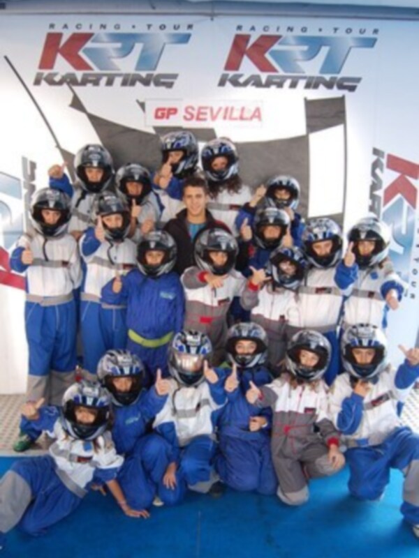 Grupo de niños en trajes de karting posando en el GP Sevilla Karting con banderas de KRT en el fondo.