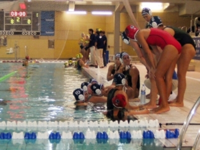 Equipo de natación listo para competir en una piscina interior, con nadadores en trajes de baño y gorros de natación, preparándose para el inicio de una carrera.