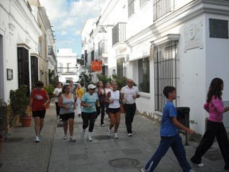 Personas corriendo en una calle con edificios blancos y azules.