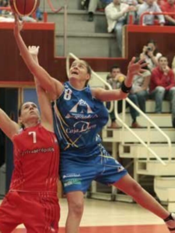 Jugadores de baloncesto en acción durante un partido en un estadio lleno de espectadores.