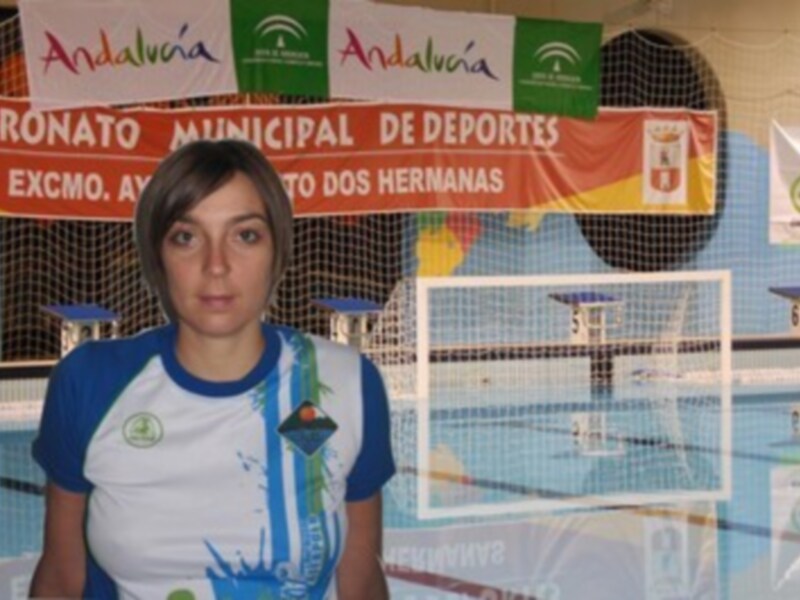 Persona en uniforme de waterpolo frente a una piscina con redes y pancartas de Andalucía y el Patronato Municipal de Deportes.
