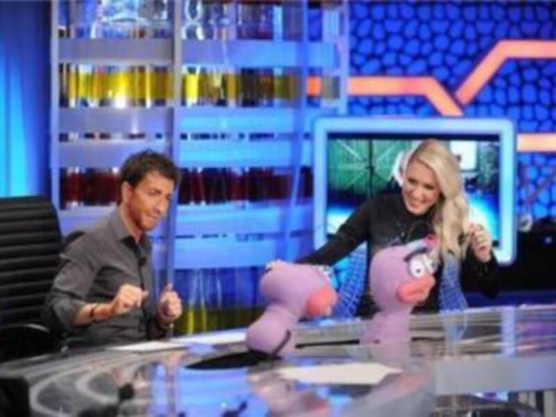 Un hombre y una mujer en un set de televisión, con el hombre sosteniendo un objeto rosa.