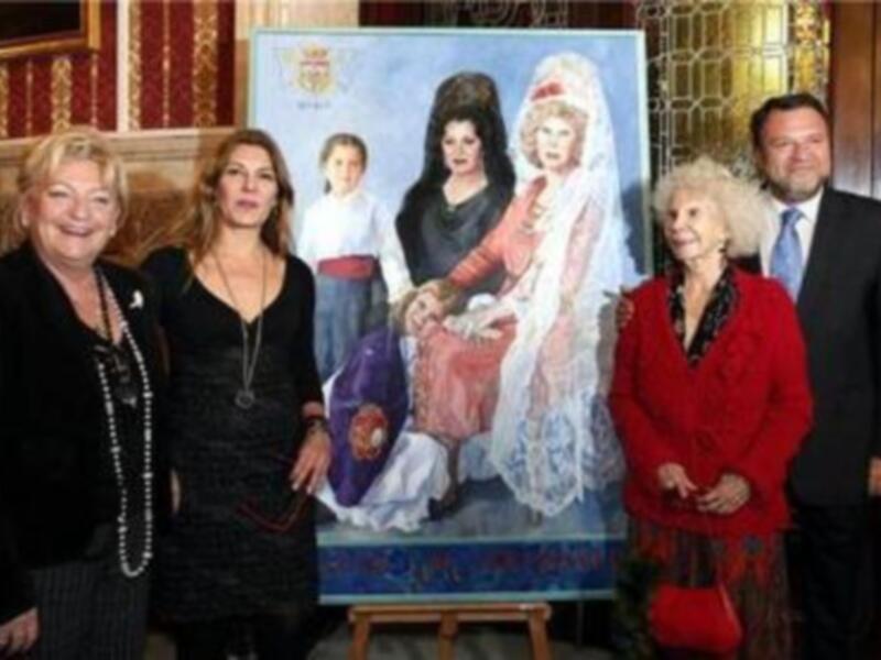 Una familia posando junto a un retrato de una mujer vestida de manera tradicional, posiblemente en un evento cultural o familiar.