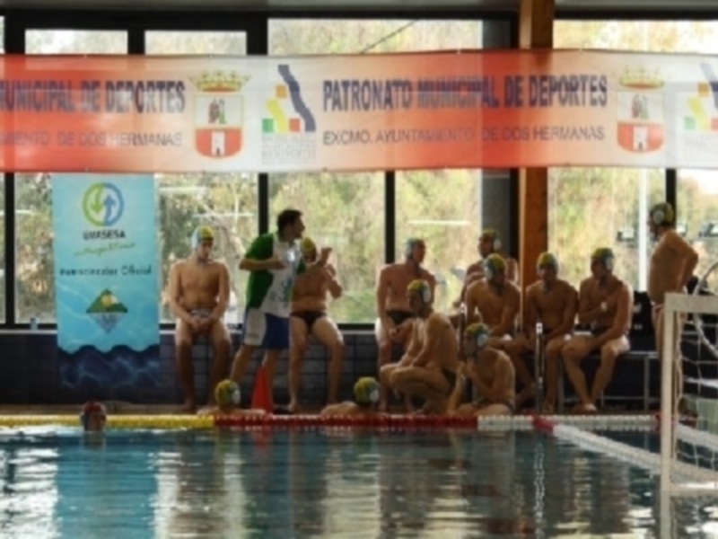 Carrera de natación en una piscina cubierta, con nadadores y espectadores observando la competencia. La imagen muestra un ambiente deportivo en un polideportivo municipal, con banners que indican la participación del Patronato Municipal de Deportes.