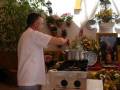 Un hombre cocina en una estufa de gas, con flores y plantas alrededor.