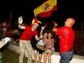Celebración nocturna con bandera española y fanáticos en uniforme rojo.