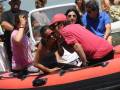 Un hombre y una mujer se besan en un bote inflable rodeado de otras personas en una celebración al aire libre.