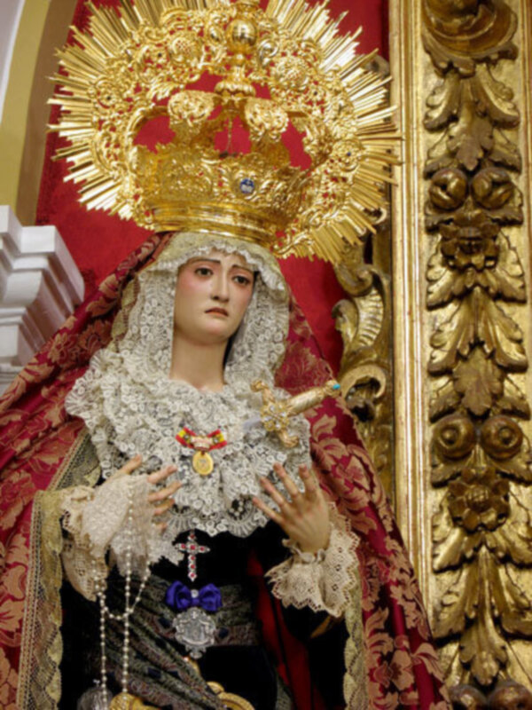 Estatua religiosa con vestimenta dorada y roja, coronada con una corona de rayos dorados.
