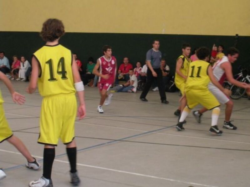 Un equipo de baloncesto en cancha, jugadores con jerseys amarillos y rojos, observando a un jugador del equipo contrario.
