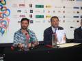 Tres hombres en una conferencia de prensa, sentados detrás de un mostrador con botellas y copas. El fondo es una pantalla con logos de diferentes empresas.