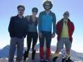 Cuatro personas posan en la cima de una montaña con el cielo azul claro.