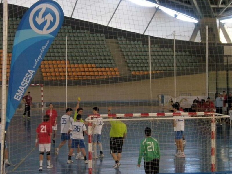 Jugadores de fútbol en una cancha interior con una bandera azul y blanca en el fondo.