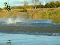 Un hombre realiza una maniobra de wakeboard en un lago, saltando alto y produciendo una gran onda de agua detrás de él. La imagen captura el momento de la acrobacia en movimiento, destacando la habilidad y el estilo del deportista.