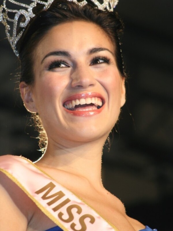 Una candidata a Miss sonríe radiante, luciendo una corona de diamantes y una sash que dice 'Miss'.