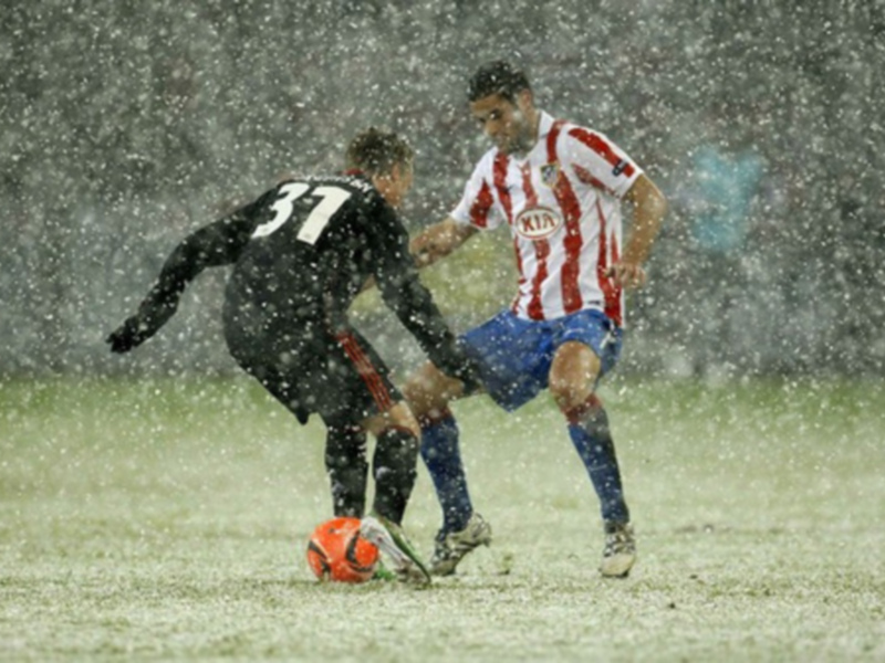 Dos jugadores de fútbol luchan por el balón en un campo nevado durante una tormenta de nieve.