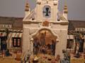 Vista de una iglesia colonial con detalles artísticos y una cruz en el techo, situada en un entorno arqueológico con figuras humanas y animales en el suelo.