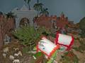 Un precioso y detallado escenario navideño con figuras de animales, un carro blanco con detalles rojos y una arquitectura medieval en el fondo.