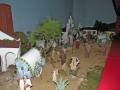 Una escena navideña con figuras de madera en una representación de un pueblito. Hay carros, árboles y figuras vestidas con ropa de época. La escena está iluminada por una luz azul que simula la noche.