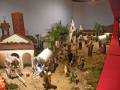 Un bello escenario de pesebre navideño con figuras humanas y animales, una iglesia en el fondo y un cielo nublado.