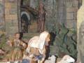 Escena navideña con figuras de madera, un pastor con ovejas y un hombre en el fondo.