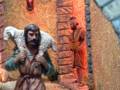Un pastor con una oveja en la espalda y otro pastor con un cuchillo en la mano. La escena parece ser de una escena religiosa o histórica, con un muro rojizo y una linterna encendida en el fondo.
