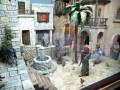 Un entorno medieval con una fuente de piedra, un burro y figuras humanas en trajes antiguos.