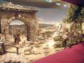 Escena navideña con figuras de animales y personas en un entorno rural, incluyendo una carreta y un arco de piedra.