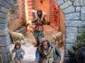 Un niño camina hacia una puerta de piedra mientras un anciano con una capa azul y un niño pequeño lo siguen. Un cordero está en el suelo cerca de ellos, y hay otros personajes en la escena.