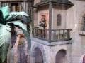 Miniatura de una estructura medieval con una figura en el balcón, rodeada de plantas tropicales.
