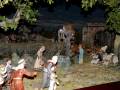 Escena navideña con personajes y animales, incluyendo pastores, ovejas y un arco de piedra.