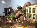 Un entorno navideño con figuras de personas y animales en una escena de la vida de Jesús, rodeadas de rocas, plantas y una casa en el fondo.