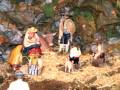 Escena navideña con figuras de madera en un entorno montañoso, incluyendo un bebé en brazos, animales como ovejas y cerdos, y personajes vestidos con ropa de época.