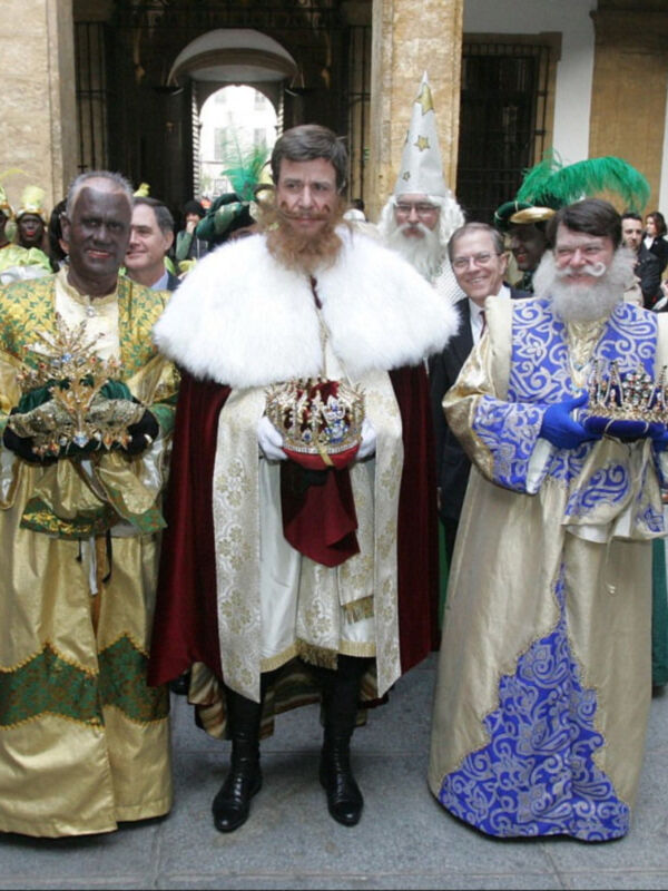 Los personajes en traje medieval posan con joyas y coroas, frente a un edificio histórico.