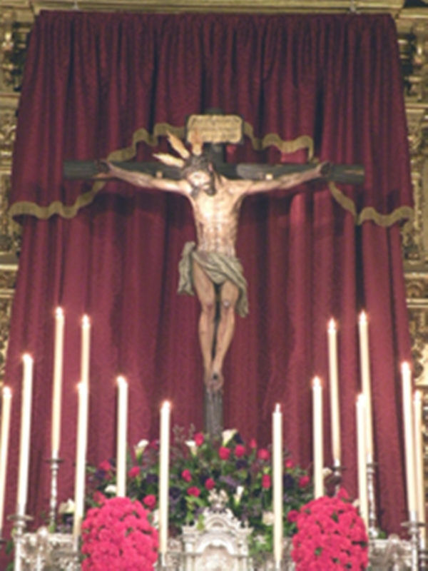 Crucifijo en una iglesia, rodeado de velas y flores rojas.