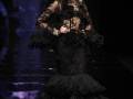 Una modelo con un vestido negro de encaje y volantes, posando en la pasarela.