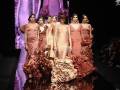 Modelos con vestidos de colores distintos caminan por la pasarela en un desfile de moda.