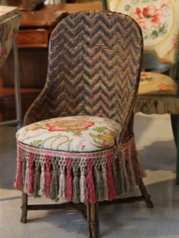 Silla de estilo vintage con patrón de zigzag en el respaldo y tapizado floral en la silla. El respaldo está cubierto con un tejido de lana con flecos en la parte inferior.