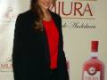 Elena Furiase posa en un evento de la marca Miura, con un fondo que muestra una botella de licor rojo.