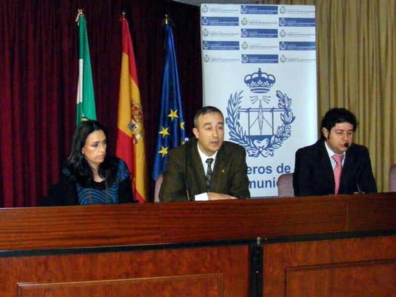 Una conferencia de prensa en un salón con tres personas en el escenario, frente a una bandera española y la bandera de la Unión Europea, con un letrero que dice 'Departamento de Defensa de la Comunidad Autónoma de Madrid'.